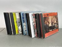 Photo showing a row of 14 music CDs in jewel cases, viewed from an angle showing the spines mostly with visible titles and artwork.