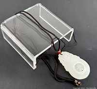 Front view of the white jade pendant displayed on a transparent stand, showing overall shape and cord.