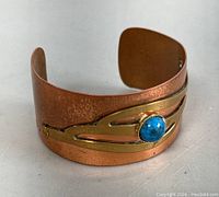 Front angle view of copper and brass cuff bracelet showing turquoise colored stone and tarnish details