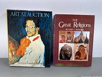 Two hardcover books standing upright showing front covers: 'Art At Auction: The Year At Sothebys 1980-81' with a painted portrait dust jacket, and 'The Great Religions' with maroon cover and religious images.