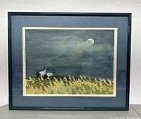 Full framed artwork showing two cranes in grass under a moonlit sky within a dark frame and white matting.
