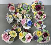 Photo of 13 porcelain floral decorative pieces showing the delicate hand-made flowers arranged in various small vases and bases.