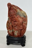 Frontal view showing detailed carving of the elderly figure on multicolored Shoushan stone mounted on black wooden base.