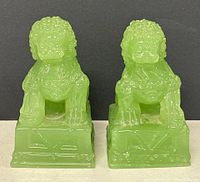 Front view of pair of green resin Foo dog figurines on square bases with detailed facial features and textured manes.