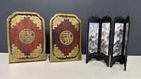 Front view of bookends showing wood and brass decoration and folding screen beside.