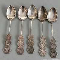 Front view of five silver spoons showing oval bowls and Chinese character handles