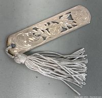 Close-up photo of a single sterling silver decorative bookmark with floral cutout pattern and silver tassel showing slight tarnish.