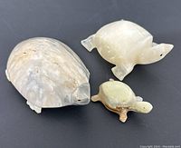 Three stone turtle figurines of varying size on black surface, showing top and side views.