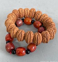Photo showing two expandable bracelets: one with carved nut beads, the other with red-orange carnelian beads and small black beads.