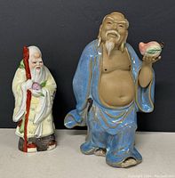 Front view of two Chinese porcelain figurines. Taller figurine in blue robe holds a peach. Smaller figurine holds a red staff.