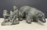 Two Inuit resin figurines side by side, bear and human scene with fire.