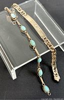 Close-up image of both bracelets displayed on clear stand, focusing on details including clasp, stones, and engraving.