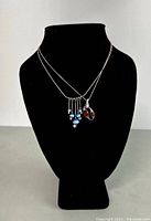 View of both necklaces displayed on black bust, showing pendants and chains.