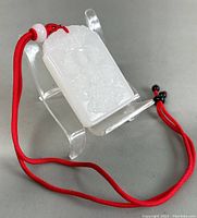Front view of white jade rectangular pendant on clear stand with red cord.
