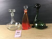 Photo showing all three decanters side by side: clear round, red-orange triangular, and green duck-shaped decanter.