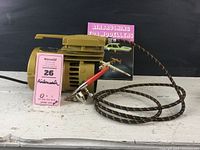 Photo of electric compressor with attached multi-color fabric hose and airbrush with red handle and side paint cup.