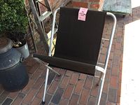 Front angled view of the folding art display stand showing black canvas sling and aluminum legs on brick flooring.