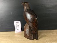 Front-side view of carved wooden eagle with yellow eyes, dark wood, standing on carved base, few marks visible.