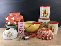 Full lot showing all items: two copper jello molds, yellow and aqua bowls, watering can, nested Decoware tins with fruit decals, red-handled kitchen tools.