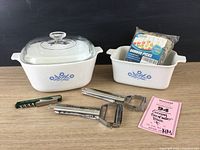 Photo showing two CorningWare Cornflower Blue casseroles with glass lids, bamboo picks, two Titan peelers, and pocket corkscrew.