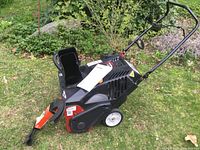 Full side view of the snow thrower showing black body, white wheels, chute, and attached manual.