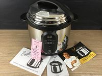 Emeril electric pressure cooker with 3 recipe books including operating manual, pictured with product label and tags.