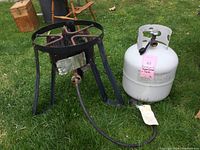 Full view of the Masterbuilt black metal propane burner and attached white propane tank on grass.