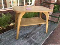 Front angle view of mid-century wood end table showing top surface, legs, and lower shelf.