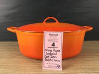 Front view of the orange enameled Dutch oven with lid on, showing round shape, handles on both sides, and lid handle.