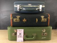 Front view of three stacked vintage suitcases: small dark blue suitcase on top, medium black suitcase in middle, large green suitcase at bottom