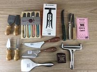 Full lot showing assortment of cheese knives, spreaders, corkscrew, and utensils on a beige wooden surface.