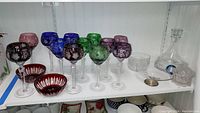 Front view of lot: assorted colored cut-to-clear crystal goblets, red bowls, clear bowl, and Wedgwood decanter with stopper