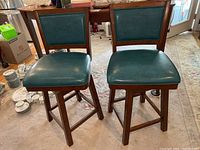 Full view of two matching vinyl padded swivel bar stools with wooden frames, showing front and seat view.