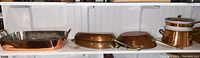 Front view of five copper cookware pieces on shelf: roasting pan, two oval pans, saucepan with lid, stackable pots