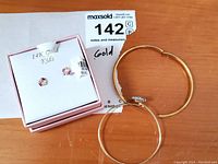 Photo of 14K gold kids birthstone earrings box with heart-shaped earrings and two gold bracelets laid on wooden surface.