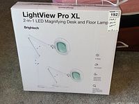 Boxed Brightech LightView Pro XL 2-in-1 LED Magnifying Desk and Floor Lamp. Box shows product images and specifications including 9 watt dimmable LED light, adjustable stand and swivel arm, scratch and heat resistant glass magnifier lens.