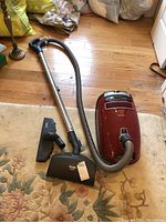 Vacuum, hose, wand and two attachments laid out on rug