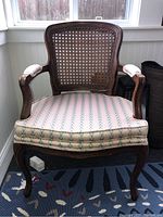 Front view of the occasional chair showing woven wicker backrest, wooden curved armrests with upholstered arm pads, and cushioned seat with patterned fabric upholstery.