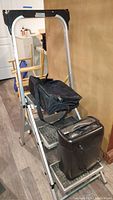 Photo showing the step ladder with the messenger bag placed on the steps and the paper shredder on the bottom step