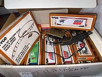 Box containing Tyco electric train tracks, wiring, control unit, and boxed train cars and accessories.