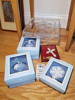 Full lot showing three boxed Wedgwood blue jasperware ornaments, Lenox Celtic cross ornament in red velvet box, and crystal footed cake stand on wooden floor.