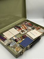 Open olive green metal case showing medals in plastic sleeves and original boxes