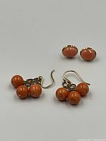 Overview of two pairs of earrings: cluster coral bead dangling earrings and oval coral cabochon studs