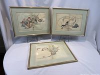 Three framed Japanese book page prints displayed, showing two framed prints standing and one lying flat on a white table.