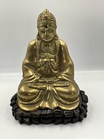 Front view of brass Buddha statue seated on wooden lotus base.