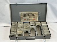 Metal carrying case open showing rows of paper-flip coins and a German banknote