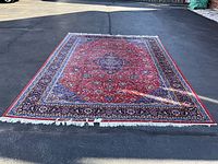 Full top-down view of rug on pavement showing red field, medallion and border