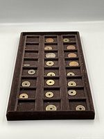 Wide angle image of 20 Asian coins laid out in a divided brown velvet storage tray, showing a mix of coins with central round and square holes.