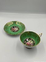 Photo of the teacup and saucer side by side showing green background, gold detailing, and floral rose motif