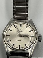 Close-up of watch dial and case front showing Omega logo, Genève marking, baton indices and domed crystal.
